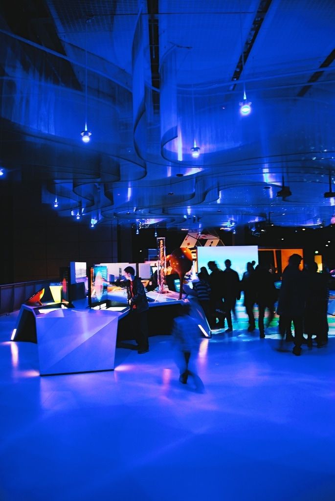 A long view through the darkened gallery towards visitors using the illuminated installations.