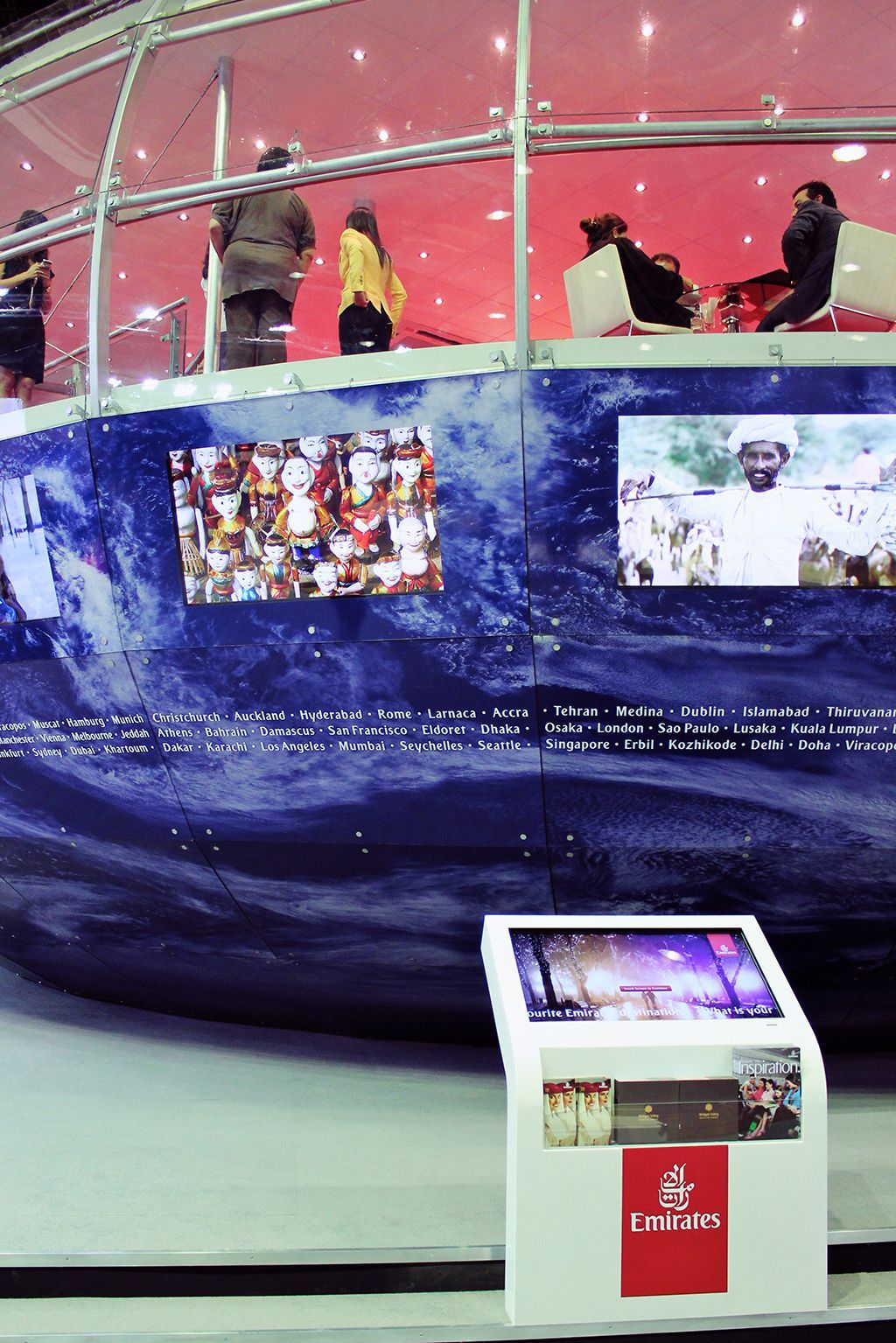An Emirates kiosk beneath a large display showing destination voting results and visitor photographs.