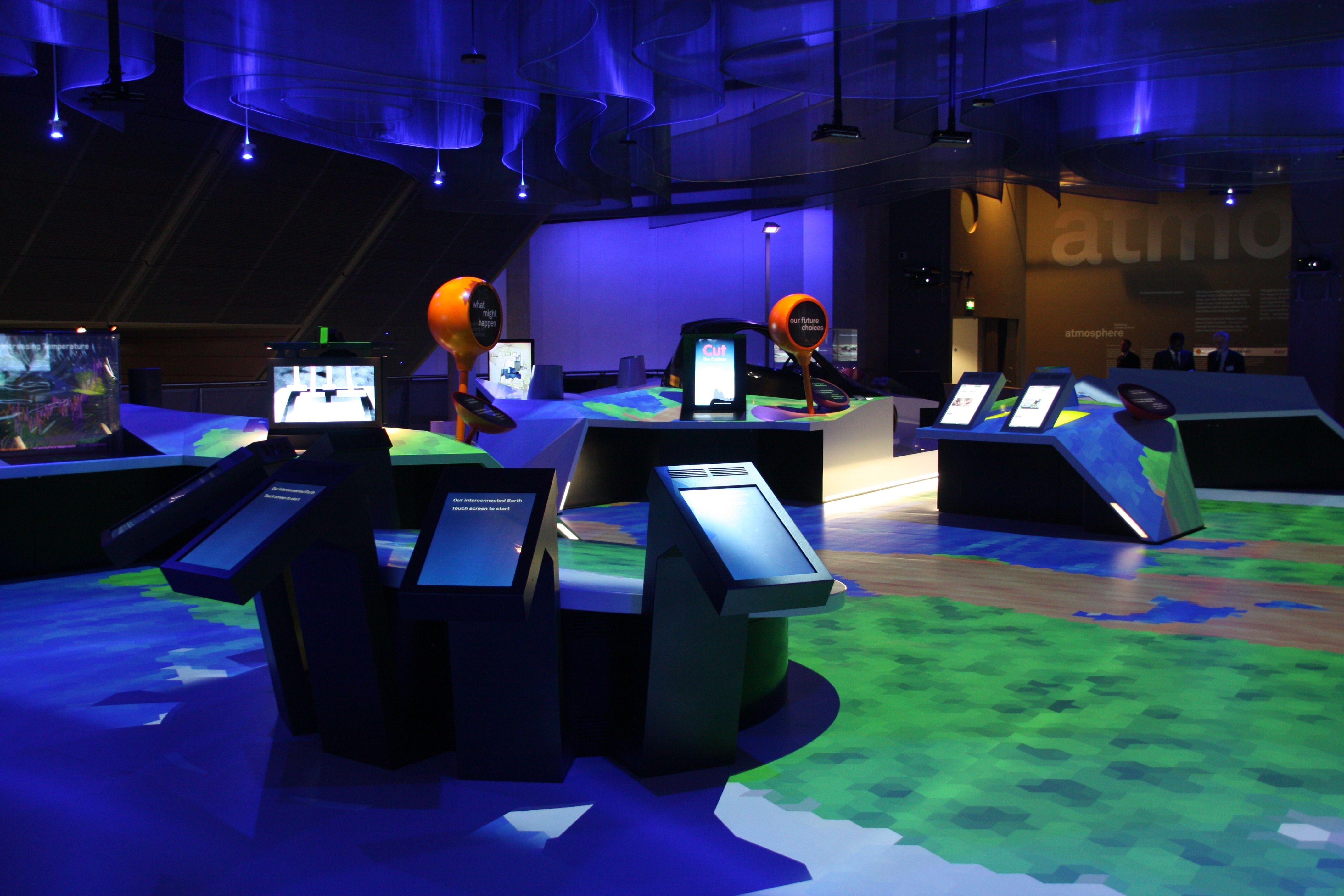 A bank of touchscreen kiosks surrounded by a floor-scale landscape projection.