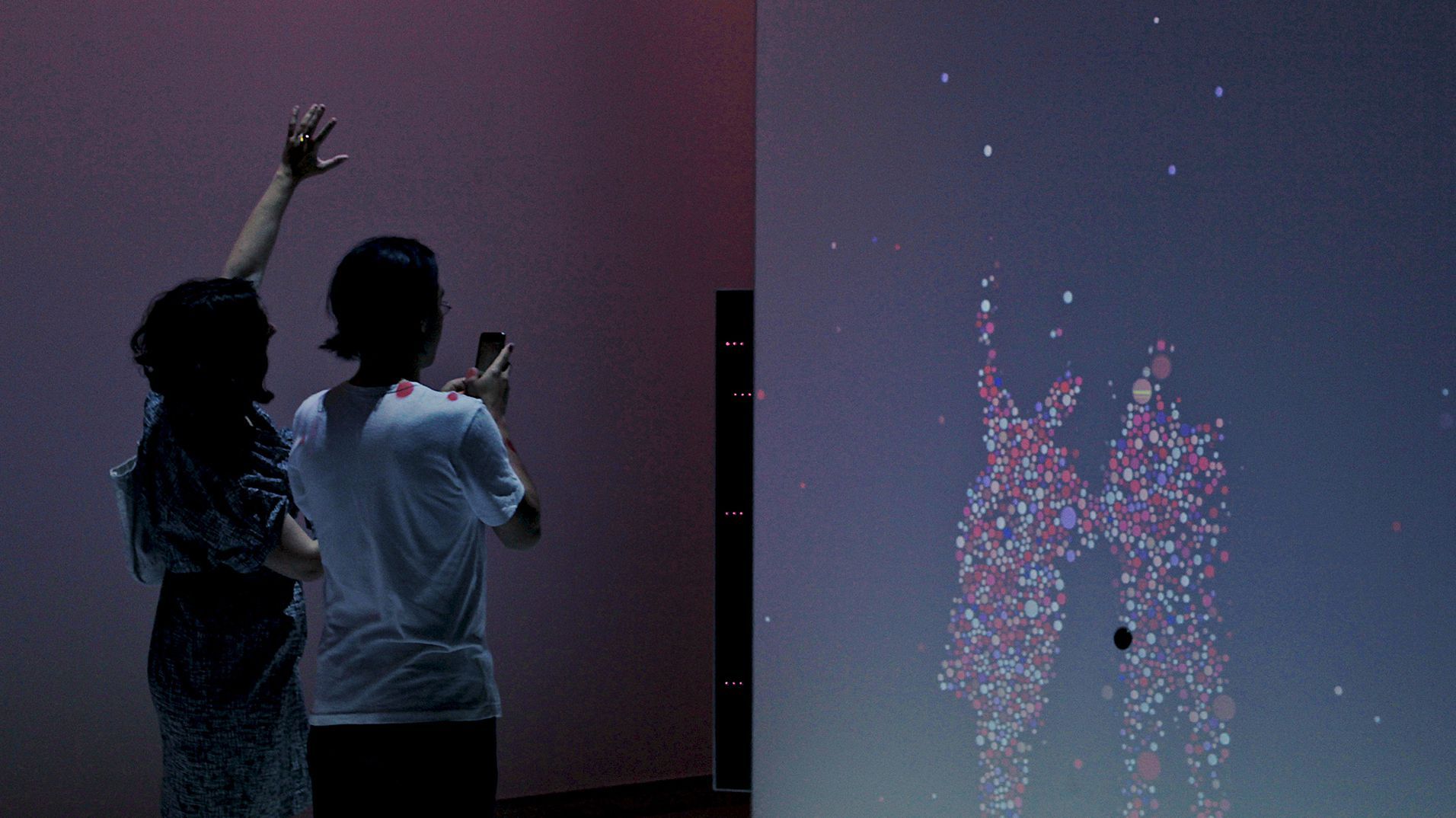 Visitors watching a human silhouette form from coloured particles in the Science Museum gallery.