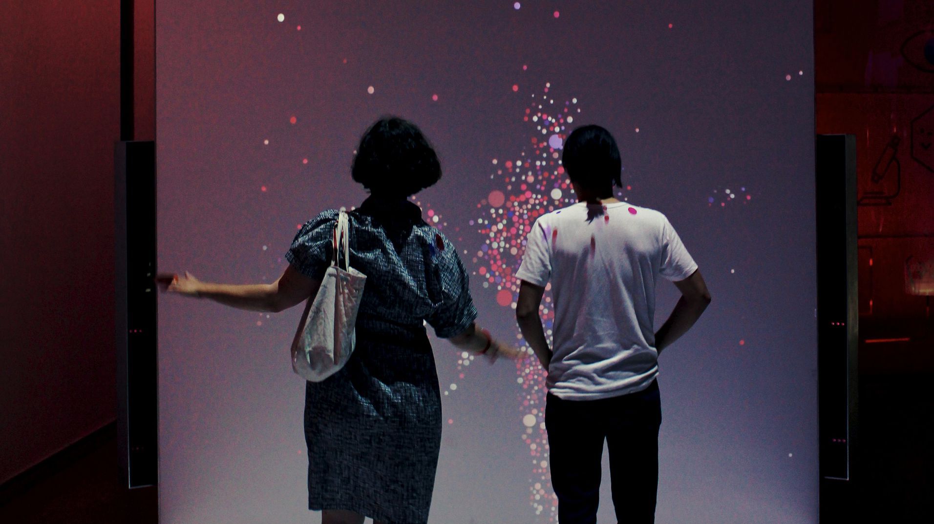 Two visitors interacting with a particle silhouette projected at human scale.